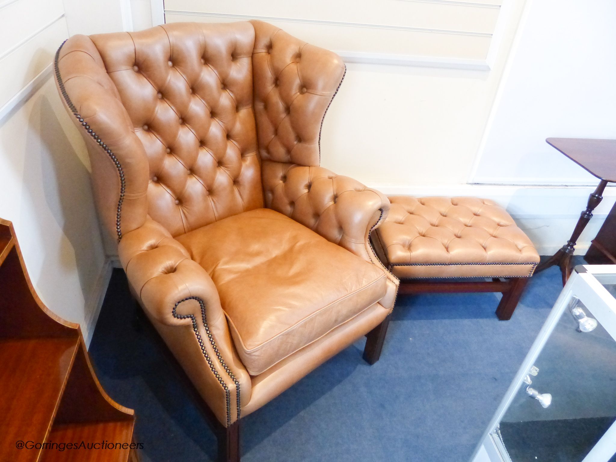 A pair of George III style buttoned tan leather wingback armchairs and two matching footstools